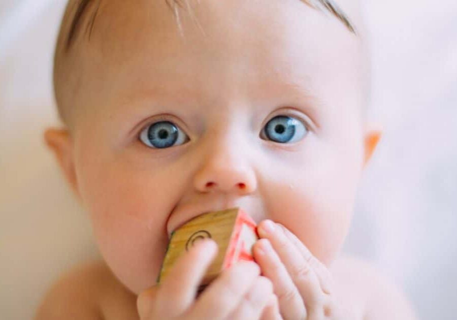 Tips on feeding your baby solids. Baby trying to put wooden block in his mouth.