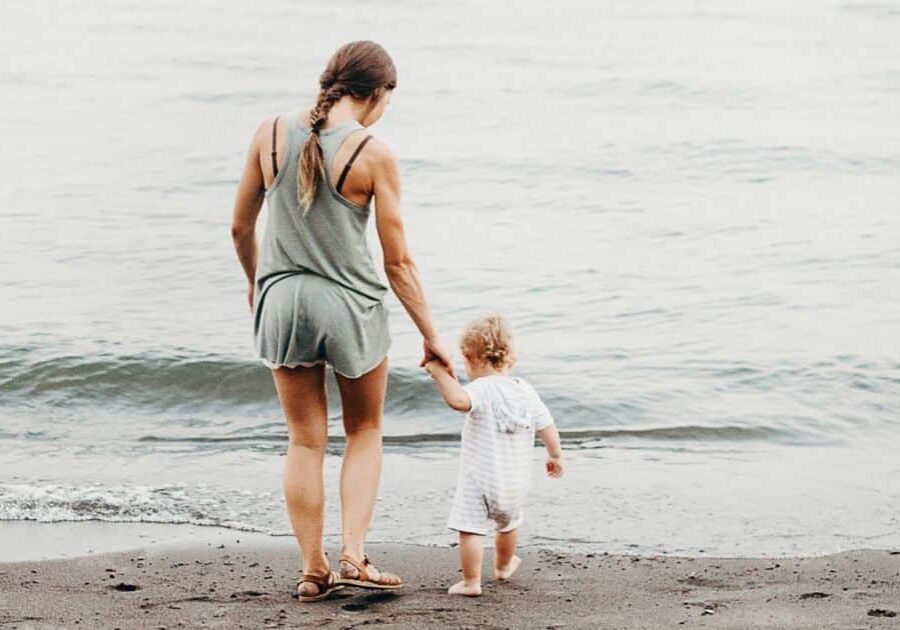 Best summer baby tips for a safe and enjoyable season. Mom & baby standing at ocean shore.